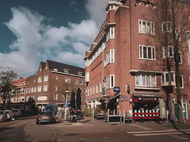 Red brick buildings in an Amsterdam neighborhood street with shops and cars on a sunny day. Buurtprofielen lezen: welke openbare cijfers typeren uw wijk